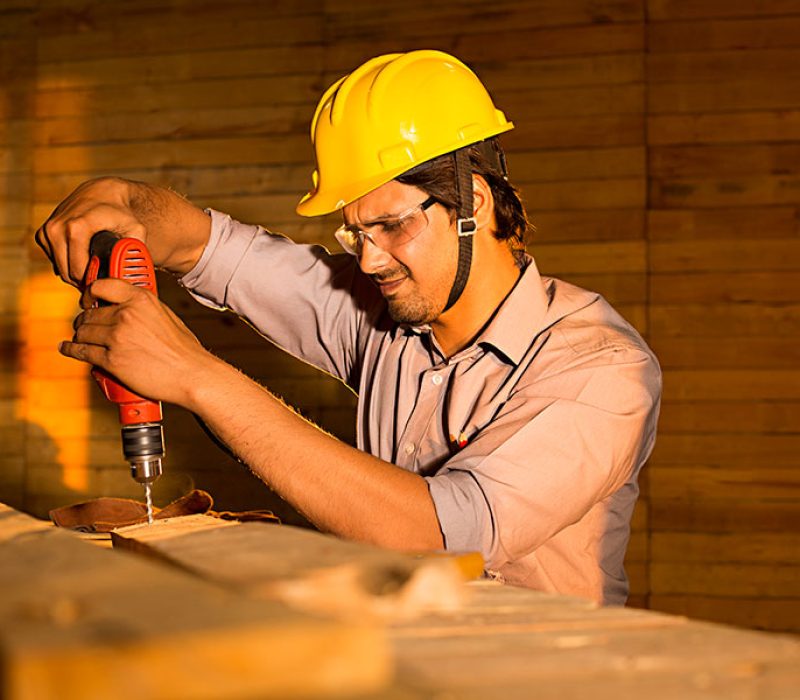 A man in a hard hat using a drill to create a door design in the smart window solution industry.